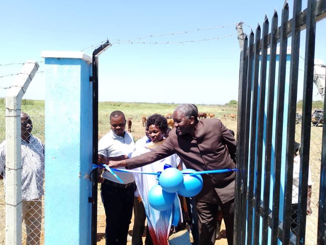 Alfred Okot Okidi, the Permanent Secretary at the Ministry of Water and Environment being helped to cut a ribbon to commission the irrigation project. Photo by Susan Nanjala.